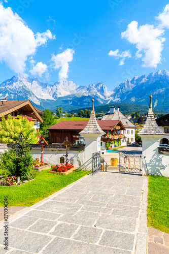 TIROL, AUSTRIA - JUL 30, 2018: Church cemetery and traditional alpine houses in village of Going am Wilden Kaiser on beautiful sunny summer day with Alps mountains in background, Tirol, Austria.