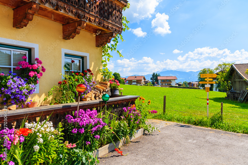 Traditional alpine house decorated with flowers in village of Going am Wilden Kaiser on beautiful sunny summer day with Alps mountains in background, Tirol, Austria