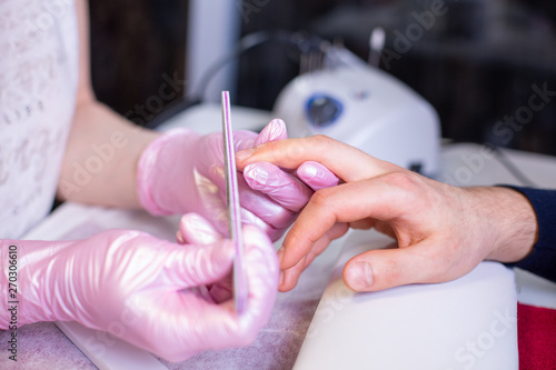 Professional manicure of male hands in a beauty salon close up. Master in gloves makes a manicure using modern technologies. Beauty concept of personal care, health, hand care.