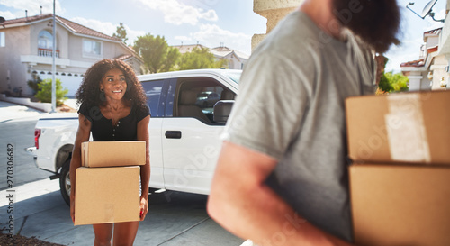 Photography interracial couple moving into new home and taking boxes out of truck