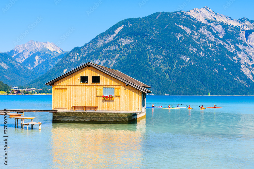 Wooden boat house and tourists on kayaks on beautiful Achensee lake on sunny summer day, Tirol, Austria