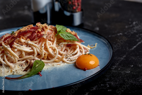 Classic pasta carbonara with yolk on a plate. Pasta laid out on a blue plate on a dark background. Concept of Italian cuisine, beautiful serving dishes, close-up.