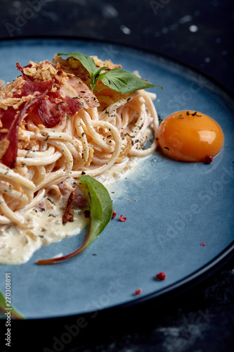 Classic pasta carbonara with yolk on a plate. Pasta laid out on a blue plate on a dark background. Concept of Italian cuisine, beautiful serving dishes, close-up.