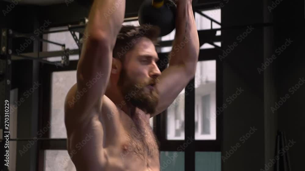 Closeup shoot of adult muscular athletic man making squats with the kettlebells indoors in the gym Closeup shoot of adult muscular athletic man making squats with the kettlebells indoors in the gym