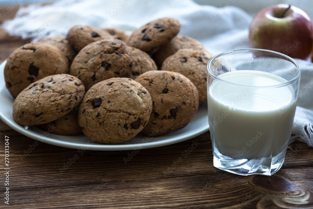 Pile of Delicious Chocolate Chip Cookies on a plate with glass of milk on wooden table Pile of Delicious Chocolate Chip Cookies on a plate with glass of milk on wooden table