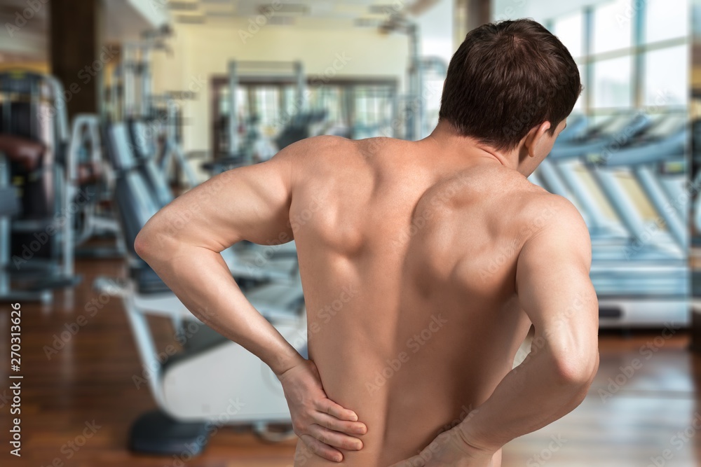Back view of shirtless man touching his aching back Back view of shirtless man touching his aching back