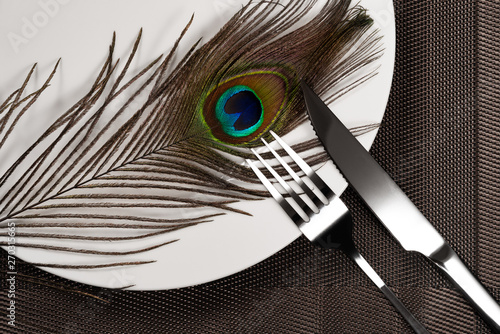 Foto fork and knife and a peacock feather on a dish concept of eating inhuman wildlif