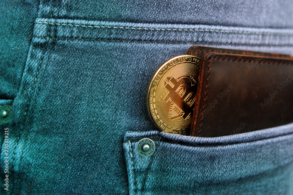 dark brown men's wallet made of high-quality genuine leather, from which you can see electronic money; golden Bitcoin is in the back pocket of men's gray jeans, tinted in turquoise color photo