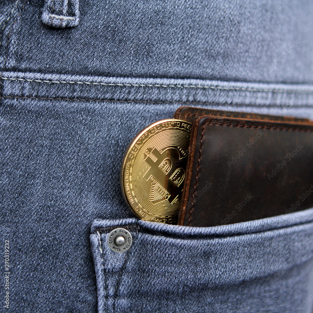 Cryptocurrency coin gold Bitcoin lies in a leather wallet in the back pocket of men's gray jeans, square, close-up Cryptocurrency coin gold Bitcoin lies in a leather wallet in the back pocket of men's gray jeans, square, close-up