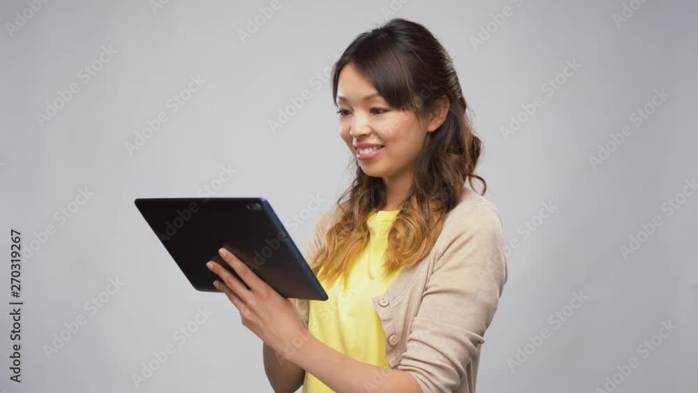 technology and people concept - asian woman using tablet computer over grey background technology and people concept - asian woman using tablet computer over grey background