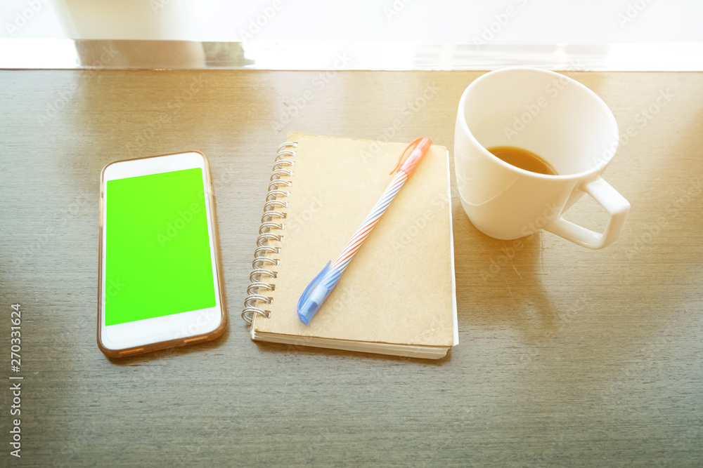 Smartphone with green screen, notebook and coffee cup on wooden table background. Business concept. Smartphone with green screen, notebook and coffee cup on wooden table background. Business concept.