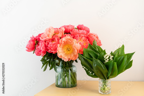 Coral peonies and spring lilies of the valley in a glass vase on wooden table.. Beautiful peony flower for catalog or online store. Floral shop concept . Beautiful fresh cut bouquet. Flowers delivery.