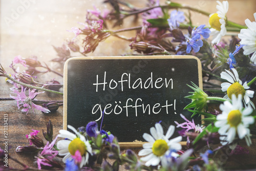 Schild. Hofladen geöffnet, umrankt von bunten Wiesenblumen photo