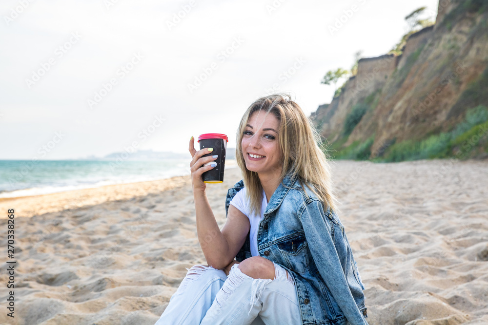young attractive female resting on the beach with caup of coffee