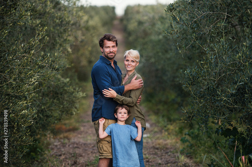 Young family with two small daughter standing outdoors in olive tree orchard.