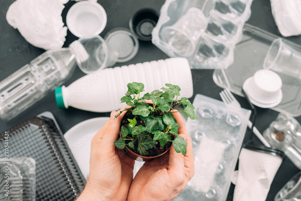 Save planet. Environment protection. Green plant in man hands over flat lay of plastic garbage. Ecology problem. Save planet. Environment protection. Green plant in man hands over flat lay of plastic garbage. Ecology problem.