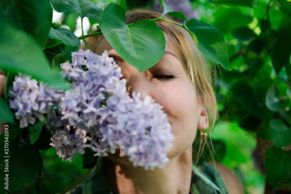 Fototapeta premium Middle age blond woman in lilac. Portrait of a woman in a flowered garden. woman in summer