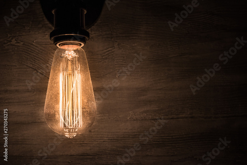 Photo Edison vintage light bulb, retro light bulb in dark room and concrete wall as ba