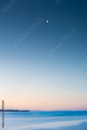 Moon over the Atlantic Ocean with purple sky and mountains in the background