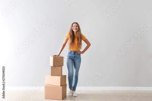 Young woman with cardboard boxes near light wall