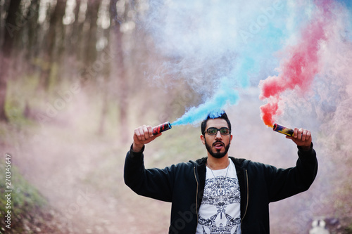 Street style arab man in eyeglasses hold hand flare with red and blue smoke grenade bomb.
