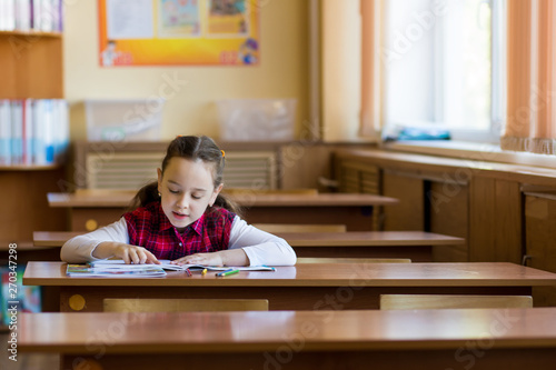 Smiling caucasian girl sitting at desk in class room and easily reads a book. Preparation for exams, tests