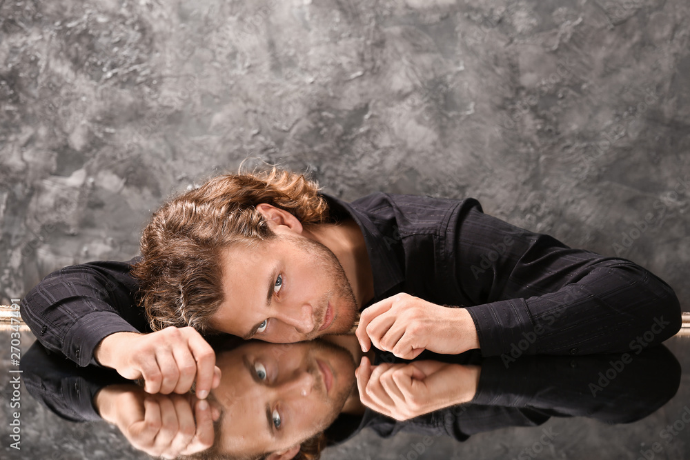 Obraz premium Stylish young man in fashionable clothes sitting at table with glass surface