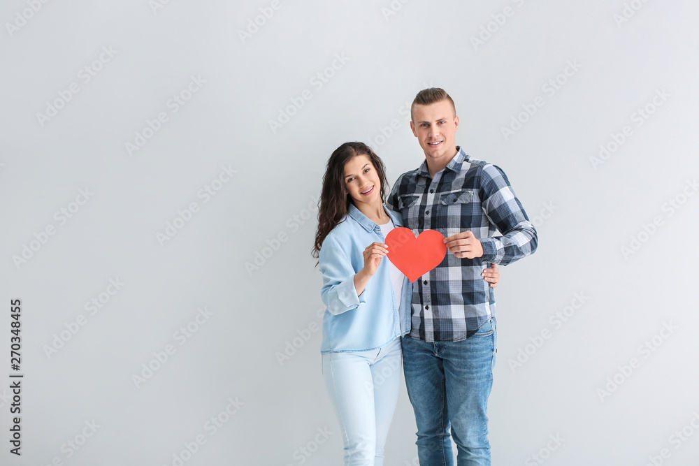 Adorable loving couple with paper heart on grey background Adorable loving couple with paper heart on grey background
