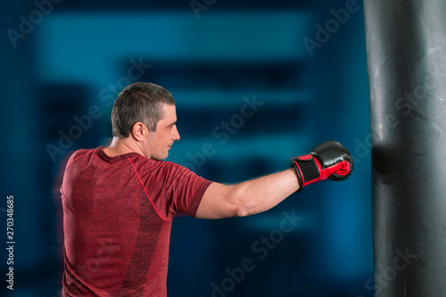young short-haired man is training in a gym with a punching bag. © igorgeiger