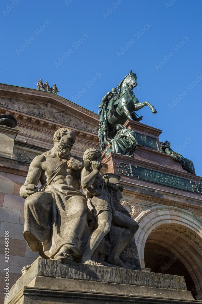 Close-up of statues (including an equestrian statue of Frederick William IV) in front of the Alte Nationalgalerie (Old National Gallery) on Museum Island in Berlin, Germany, on a sunny day.