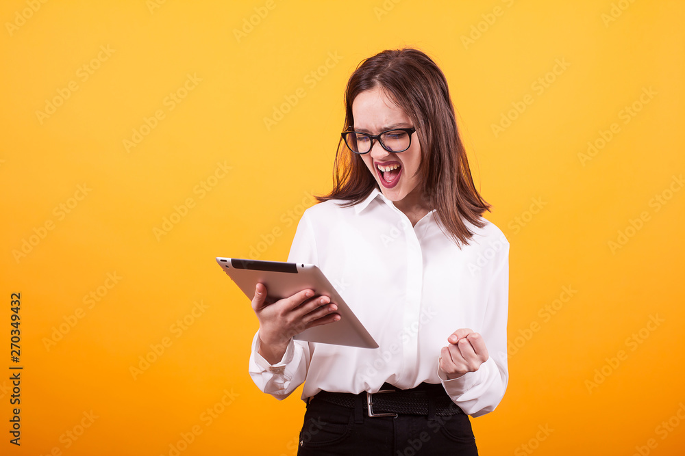 Pretty young teenager can't contain her happines and holding a tablet in studio over yellow backgroud Pretty young teenager can't contain her happines and holding a tablet in studio over yellow backgroud