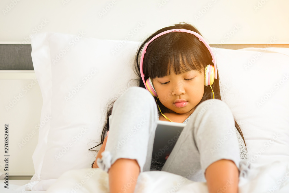 Asian girl wearing headphones Watching happy video clips, lifestyle Children's digital age Asian girl wearing headphones Watching happy video clips, lifestyle Children's digital age