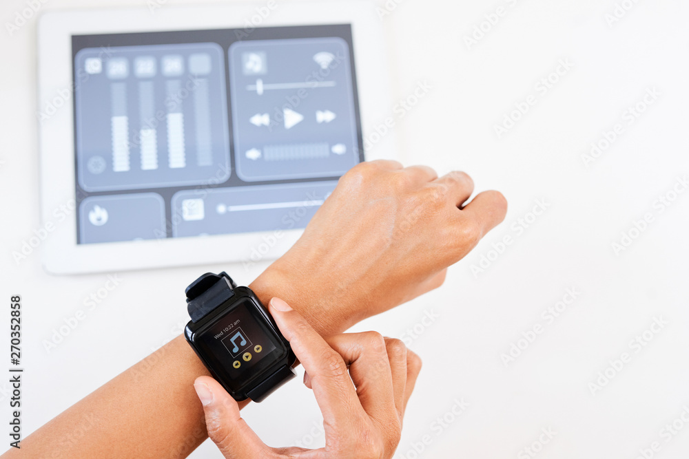 Close-up of young woman connecting smart watch on her hand with digital tablet and controlling the sound while listening to music Close-up of young woman connecting smart watch on her hand with digital tablet and controlling the sound while listening to music