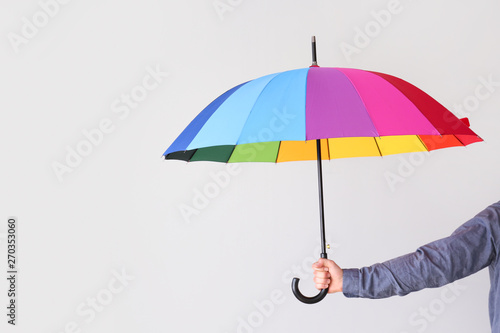 Female hand with stylish rainbow umbrella on light background