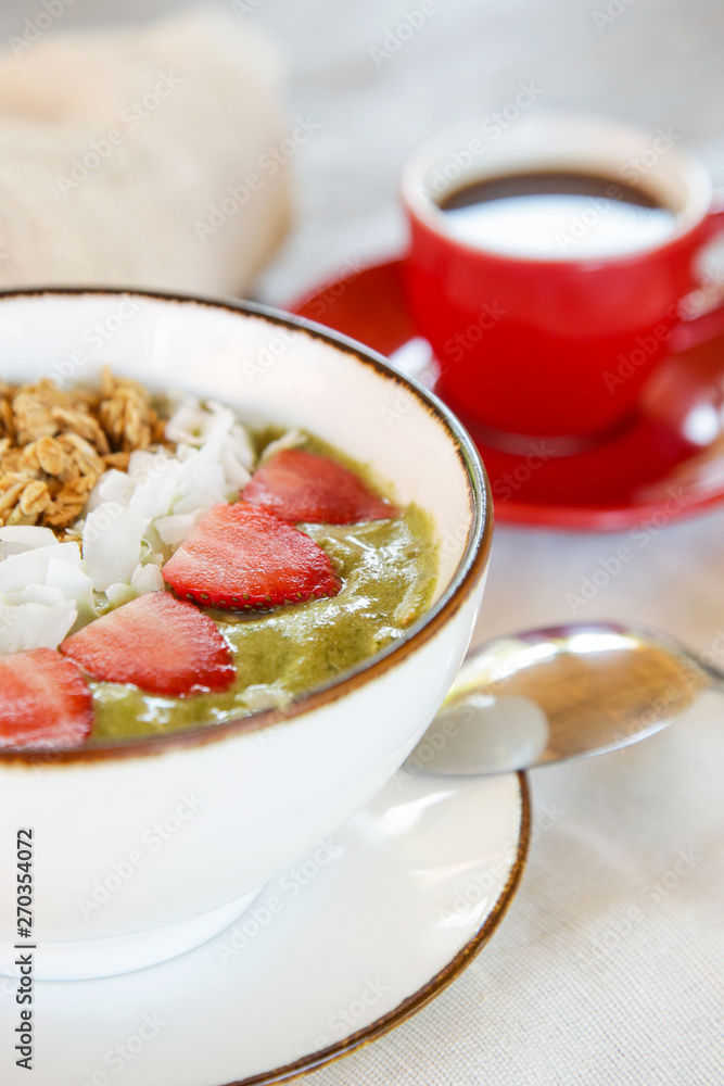 Delicious organic green smoothie bowl garnished with strawberries, sliced almonds and granola served with a cup of coffee Delicious organic green smoothie bowl garnished with strawberries, sliced almonds and granola served with a cup of coffee
