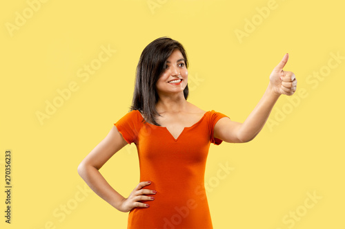 Beautiful female half-length portrait isolated on yellow studio background. Young emotional indian woman in dress showing the sing of OK. Negative space. Facial expression, human emotions concept.