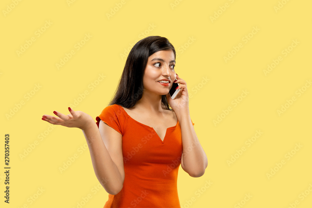 Beautiful female half-length portrait isolated on yellow studio background. Young emotional indian woman in dress talking on the phone. Negative space. Facial expression, human emotions concept. Beautiful female half-length portrait isolated on yellow studio background. Young emotional indian woman in dress talking on the phone. Negative space. Facial expression, human emotions concept.
