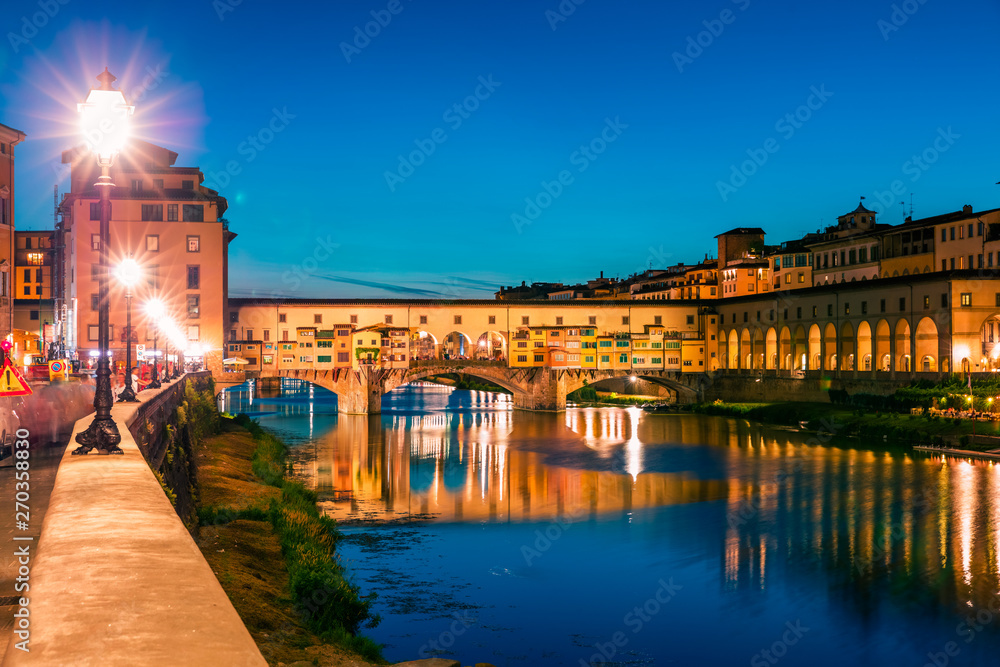 Fantastic evening cityscape of Florence with Old Palace (Palazzo Vecchio or Palazzo della Signoria) on background and Ponte Vecchio bridge over Arno river. Colorful night scene of Italy, Europe.