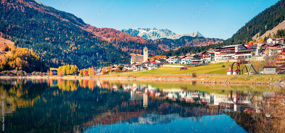 Amazing autumn panorama of Resia village and lake. Amazing morning scene of Italian Alps, South Tyrol, Italy, Europe. Traveling concept background.
