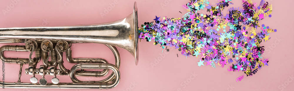 Fototapeta premium Panoramic shot of trumpet and colorful confetti on pink background