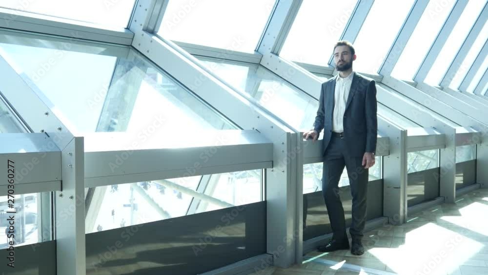 A Young Businessman with Beard on a Face stands up near a Window And Looks Out A Young Businessman with Beard on a Face stands up near a Window And Looks Out