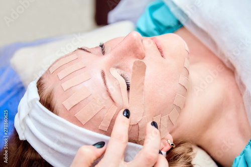 Face aesthetic taping. Facial skin care. Young woman lying with tape applications on face. Non-invasive anti-ageing lifting method for reduction of wrinkles on the forehead and the outer eye corners