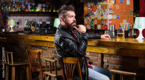 Hipster relaxing at bar with beer. Bar is relaxing place to have drink and relax. Man with beard spend leisure in dark bar. Brutal hipster bearded man sit at bar counter drink beer. Friday evening photo