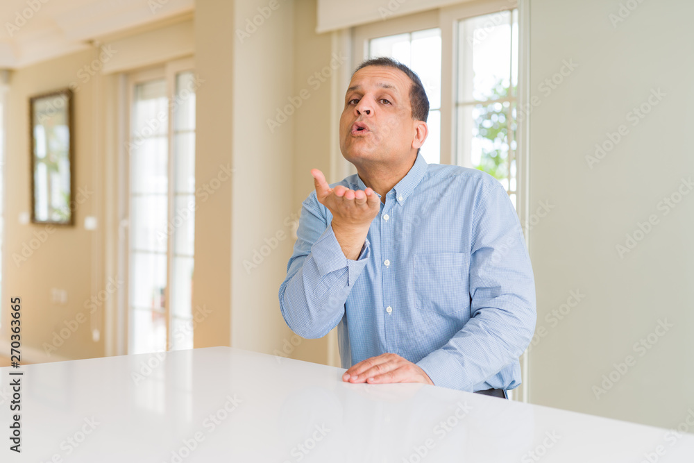 Middle age man sitting at home looking at the camera blowing a kiss with hand on air being lovely and sexy. Love expression. Middle age man sitting at home looking at the camera blowing a kiss with hand on air being lovely and sexy. Love expression.