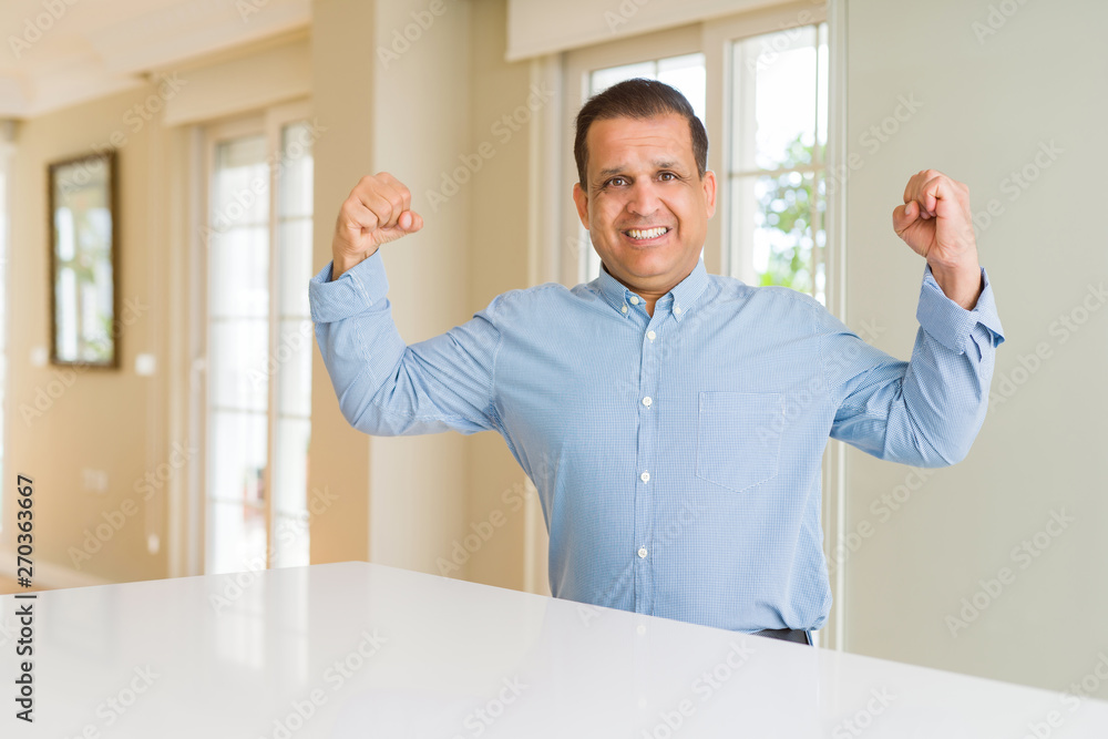 Middle age man sitting at home showing arms muscles smiling proud. Fitness concept.