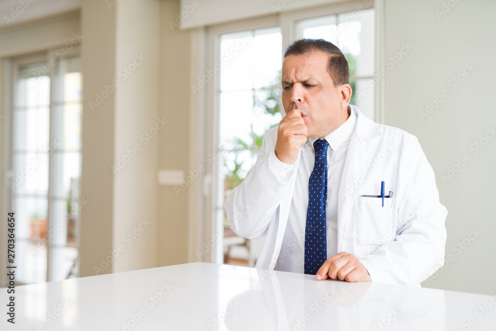 Middle age doctor man wearing medical coat at the clinic feeling unwell and coughing as symptom for cold or bronchitis. Healthcare concept.