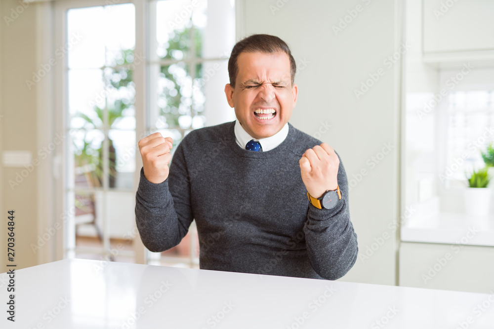 Middle age man sitting at home very happy and excited doing winner gesture with arms raised, smiling and screaming for success. Celebration concept. Middle age man sitting at home very happy and excited doing winner gesture with arms raised, smiling and screaming for success. Celebration concept.