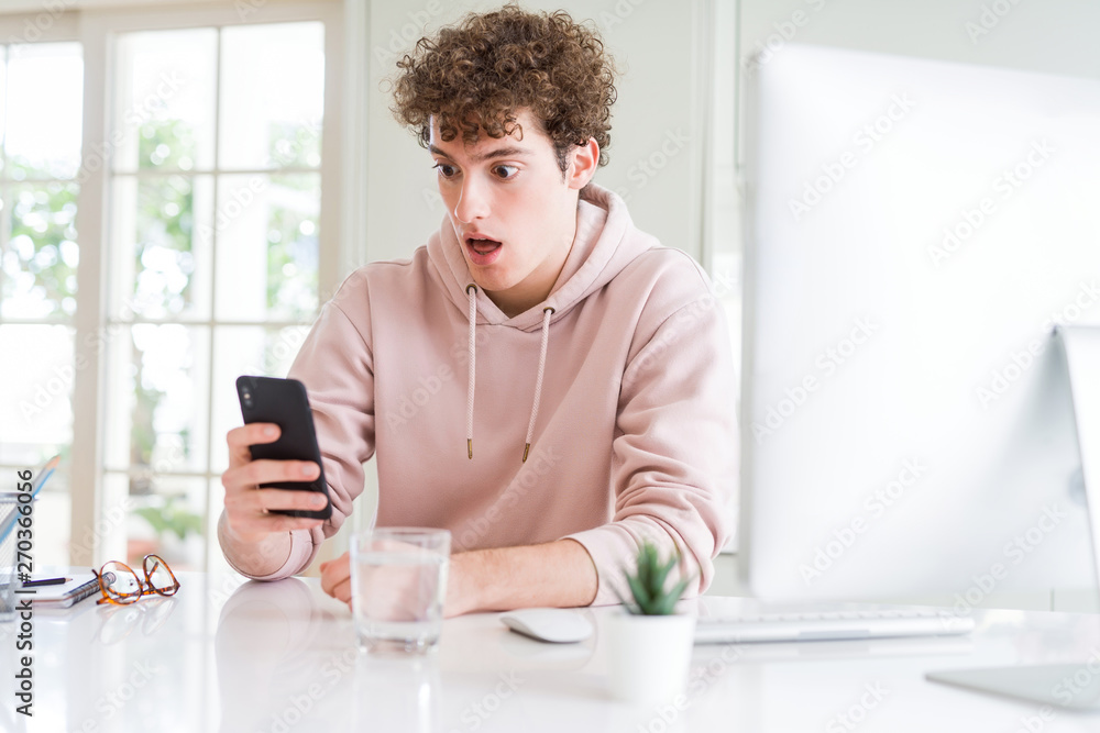 Young student man using smartphone and computer scared in shock with a surprise face, afraid and excited with fear expression