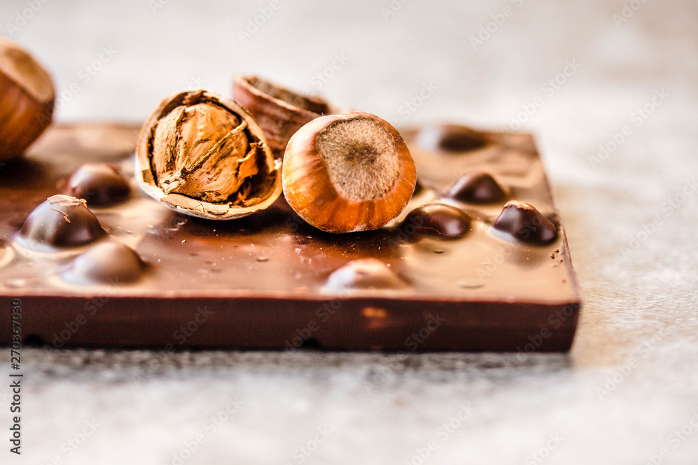 Dark chocolate bar with hazelnuts in the shell on gray background, closeup. Copy space for text. Dark chocolate bar with hazelnuts in the shell on gray background, closeup. Copy space for text.