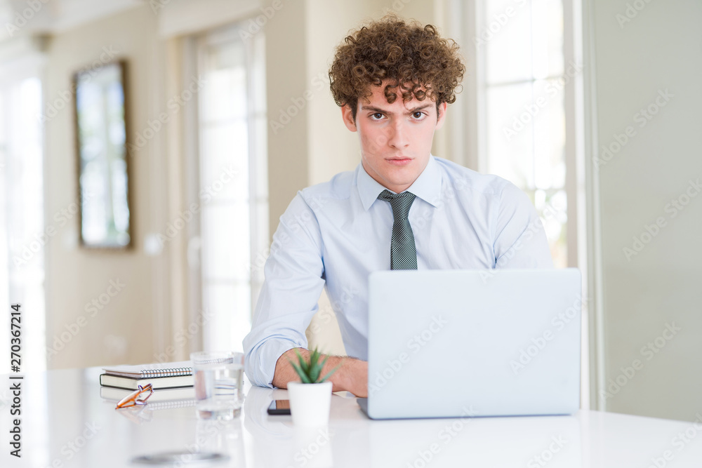 Young business man working with computer laptop at the office skeptic and nervous, frowning upset because of problem. Negative person.